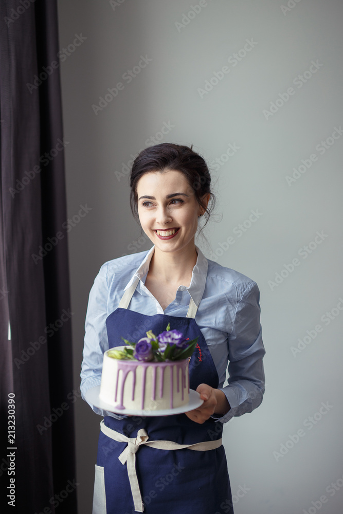 confectioner in a blue apron on a light background with a cake confectioner in a blue apron on a light background with a cake