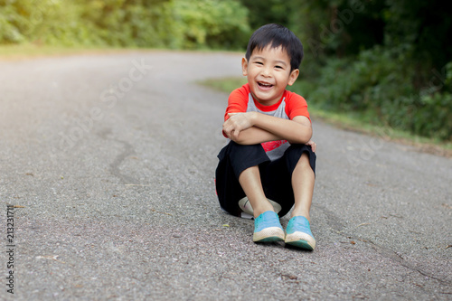 Happy Young asian cute boy sitting and Laugh on road in park.