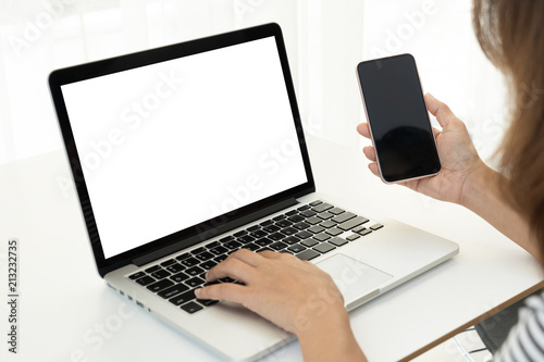 Back view. Young business woman sitting in office at table and using smartphone. On desk is laptop and tablet computer, on screen charts and graphs. Woman analyzing data. Student learning online.