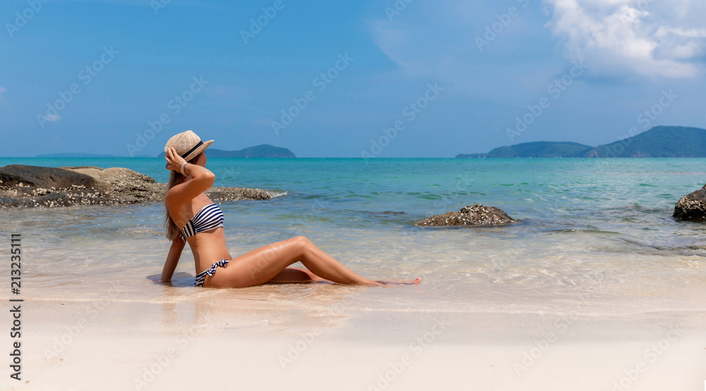 Young woman in straw hat sits on the white beach near sea