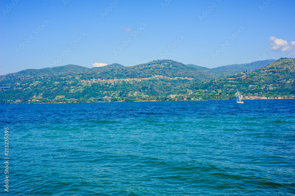 panorama of Lake Maggiore, Verbano, summer day with sun and sailing boat sailing on the horizon