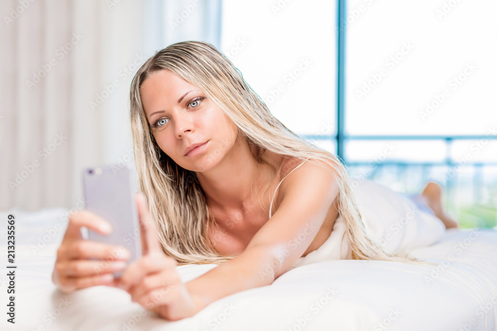 Pretty blonde woman taking selfie in the morning bed on mobile phone Pretty blonde woman taking selfie in the morning bed on mobile phone