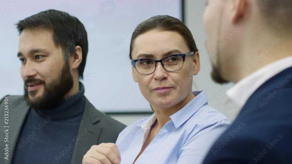 Tracking shot of mid-aged caucasian businesswoman in eyeglasses sitting with male colleagues at meeting and telling about something Tracking shot of mid-aged caucasian businesswoman in eyeglasses sitting with male colleagues at meeting and telling about something