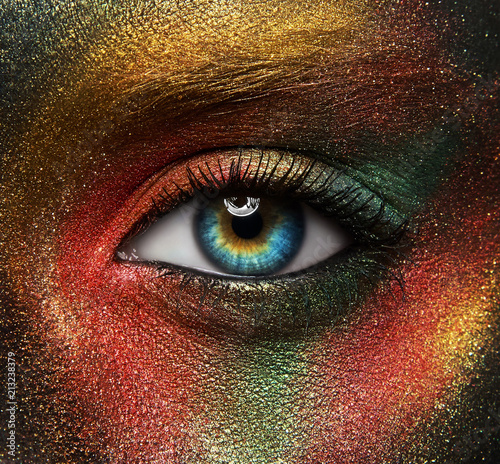 Macro and close-up creative make-up theme: beautiful female eye with yellow, orange and green paint on black skin, space and stars