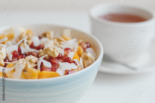 Bowl with fresh fruits and nuts served with a cup of herbal hot drink. Mango, banana, pomegranate seeds, coconut flakes, tangerine and walnut. Healthy dessert