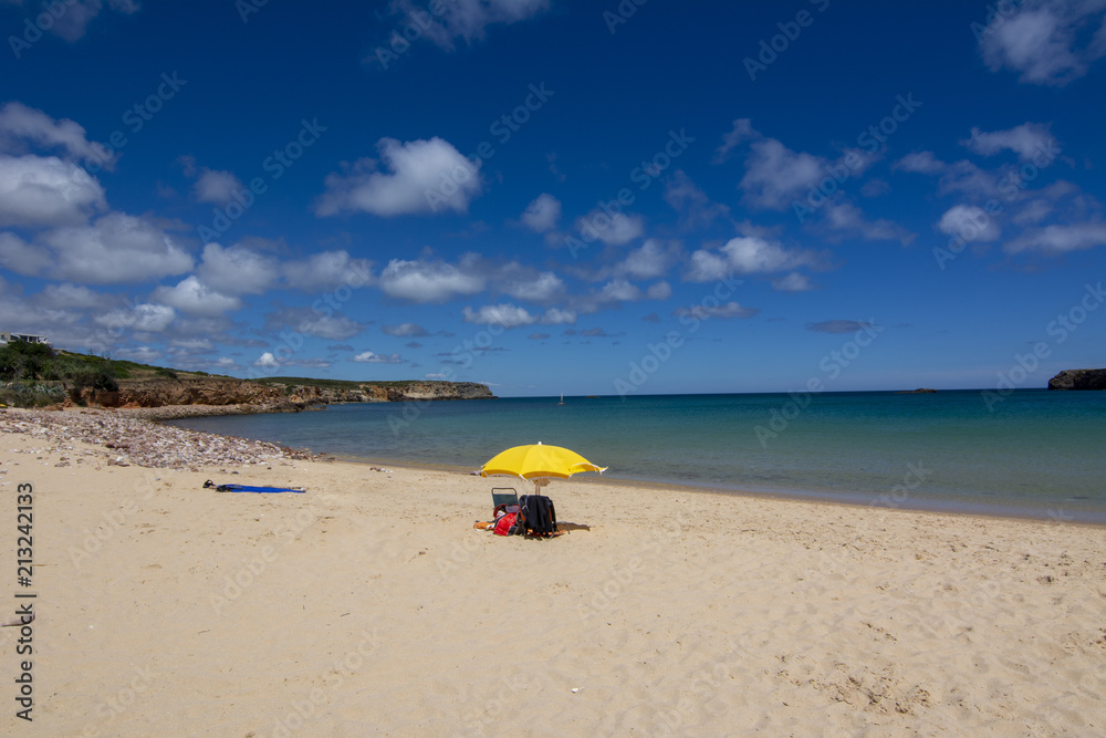 Sombrilla amarilla y útiles de playa en una bella playa del  Algarve en Portugal