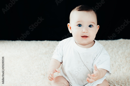 Cute smiling baby sitting in a white room near the window photo