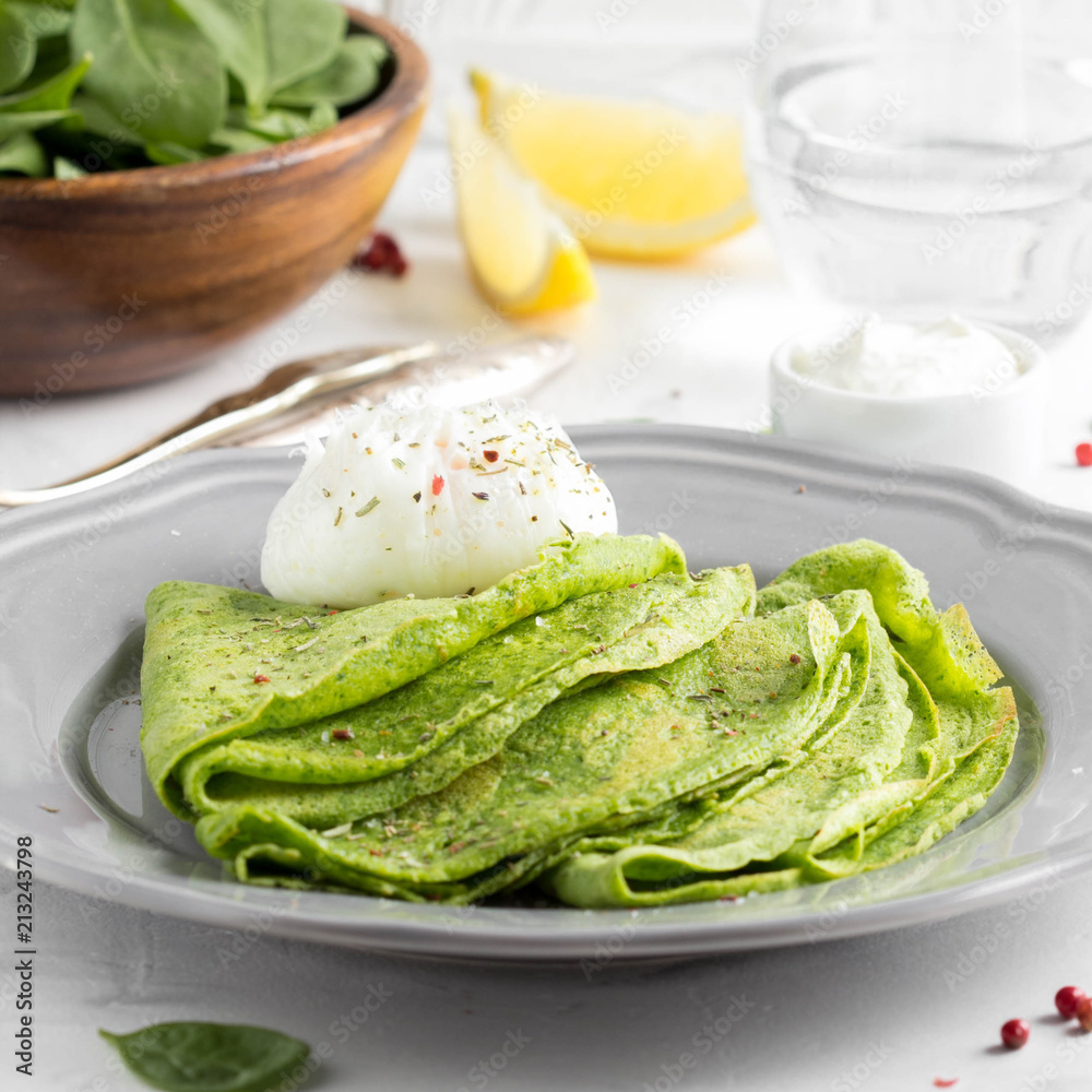 Green thin pancakes with spinach, poached egg, sour cream, lemon and aromatic herbs, delicious healthy food Green thin pancakes with spinach, poached egg, sour cream, lemon and aromatic herbs, delicious healthy food