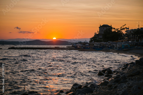 Beautiful orange sunst over the calm sea and mountains. Empty beach with umbrellas at dusk. Greece