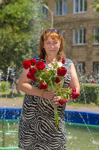 
A woman with a bouquet of red flowers stands on the background of a fountain.
