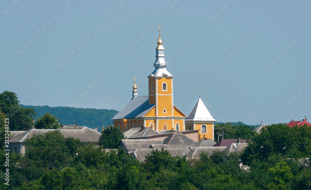 Against the background of the blue sky, the church tower with a dome of gold casting in the sun with slate roofs of houses next to it.