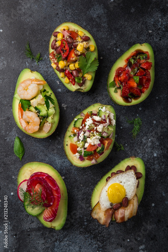  avocado halves stuffed with different toppings on dark background