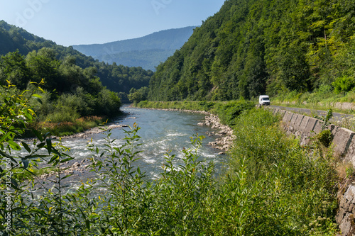 A winding road along the fast river against the backdrop of the orgomous green mountain ranges