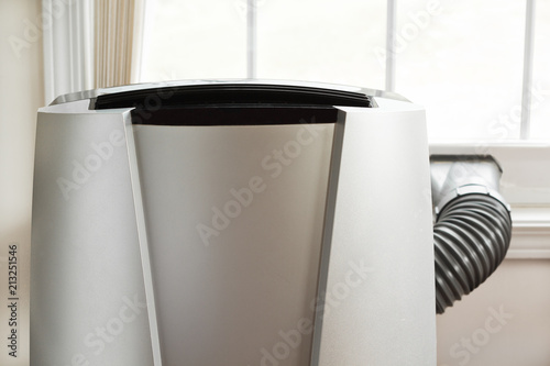 Portable air conditioner in front of brightly lit window.