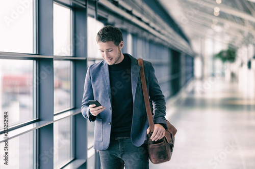 Mobile phone business man walking in airport with messenger bag using cellphone texting sms message on smartphone app - businesspeople commute lifestyle. Young professional businessman.