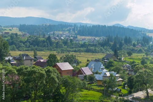 A beautiful and cozy village is located at the foot of the majestic mountains against the background of a misty sky