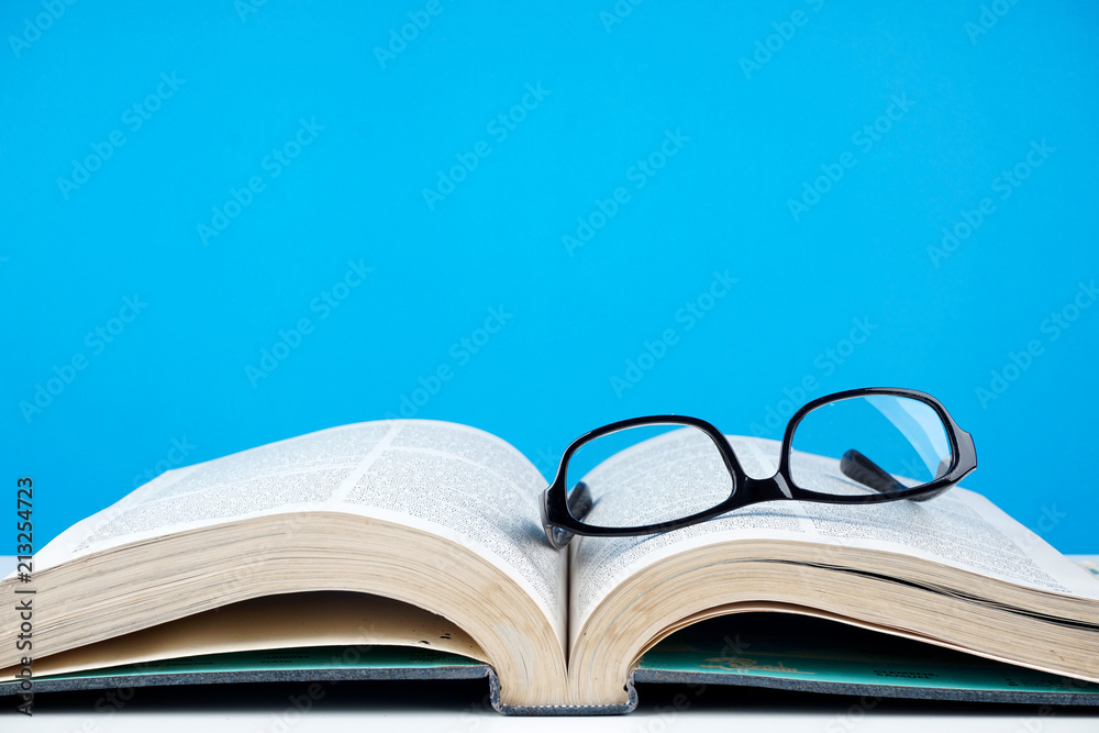 Education concept. An old book, eyeglasses over blue background Education concept. An old book, eyeglasses over blue background