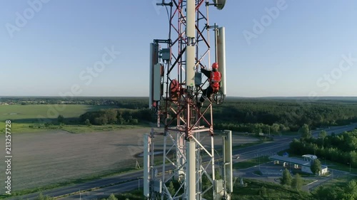 aerial view to cellular antenna, radio master working at telecommunications tower dressed on hard hat and safety vest