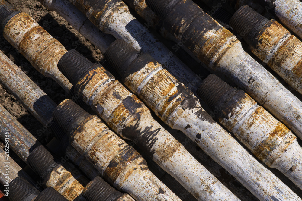 Oil Drill pipe. Rusty drill pipes were drilled in the well section. Downhole drilling rig. Laying the pipe on the deck. View of the shell of drill pipes laid in courtyard of the oil and gas warehouse. Oil Drill pipe. Rusty drill pipes were drilled in the well section. Downhole drilling rig. Laying the pipe on the deck. View of the shell of drill pipes laid in courtyard of the oil and gas warehouse.