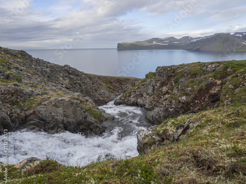 Northern wild summer landscape, View on beatuful cliffs in Hloduvik cove in west fjords nature reserve Hornstrandir in Iceland, river stream cascade, green meadow  and blue sky white clouds background photo