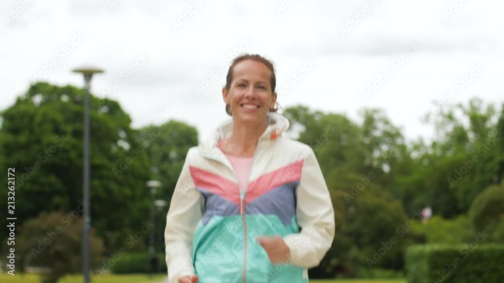 fitness, sport and healthy lifestyle concept - smiling woman running along park