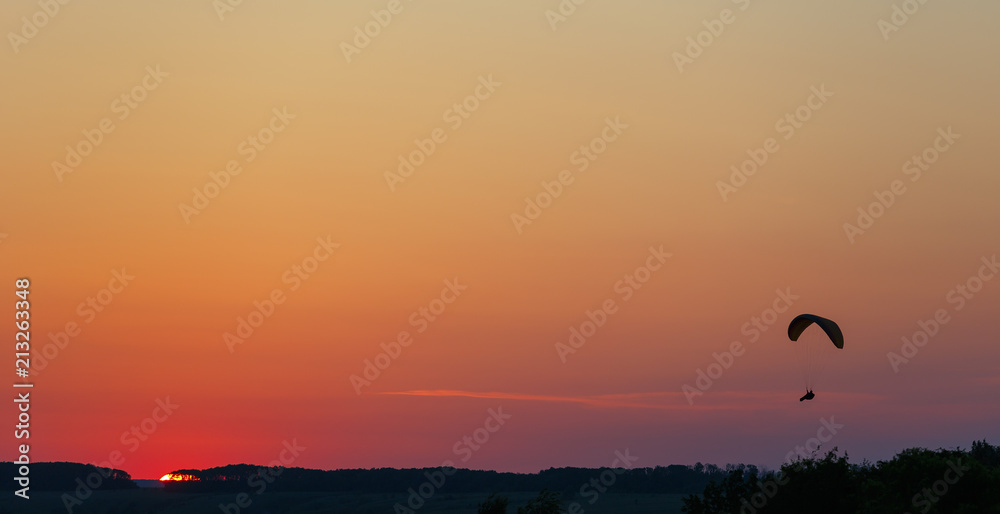 Man flight on a paraglider in a cloudless sky at sunset.