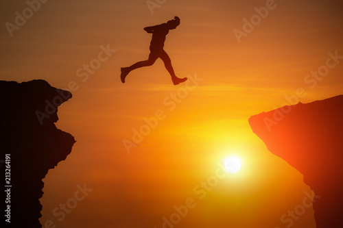 Man jumping over precipice between two rocky mountains at sunset. Freedom, Risk, Challenge, Success.