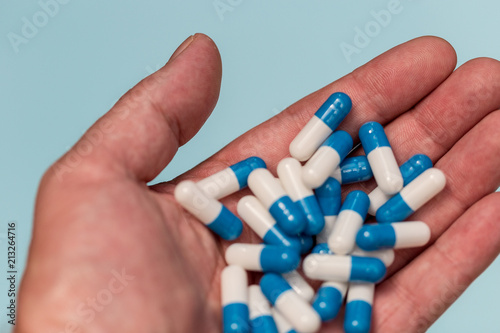Hand holding drugs pills capsules on blue background