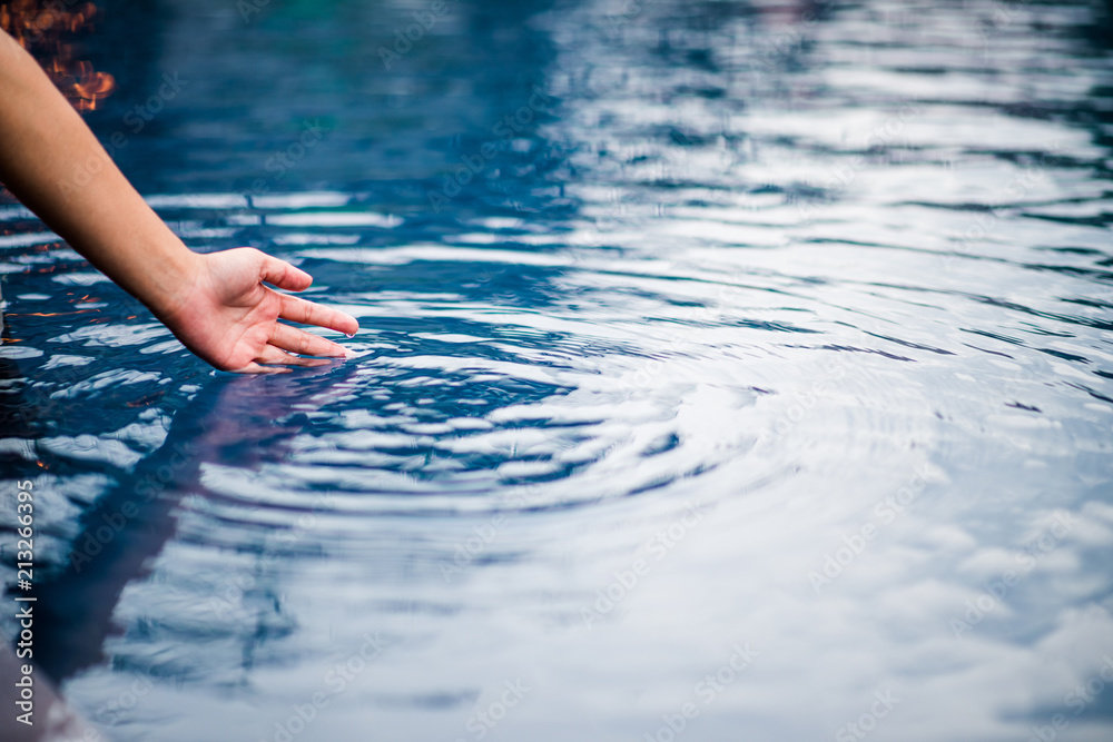 Fototapeta premium The hand that touches the blue water. The pool is clean and bright. With a drop of water on the water.