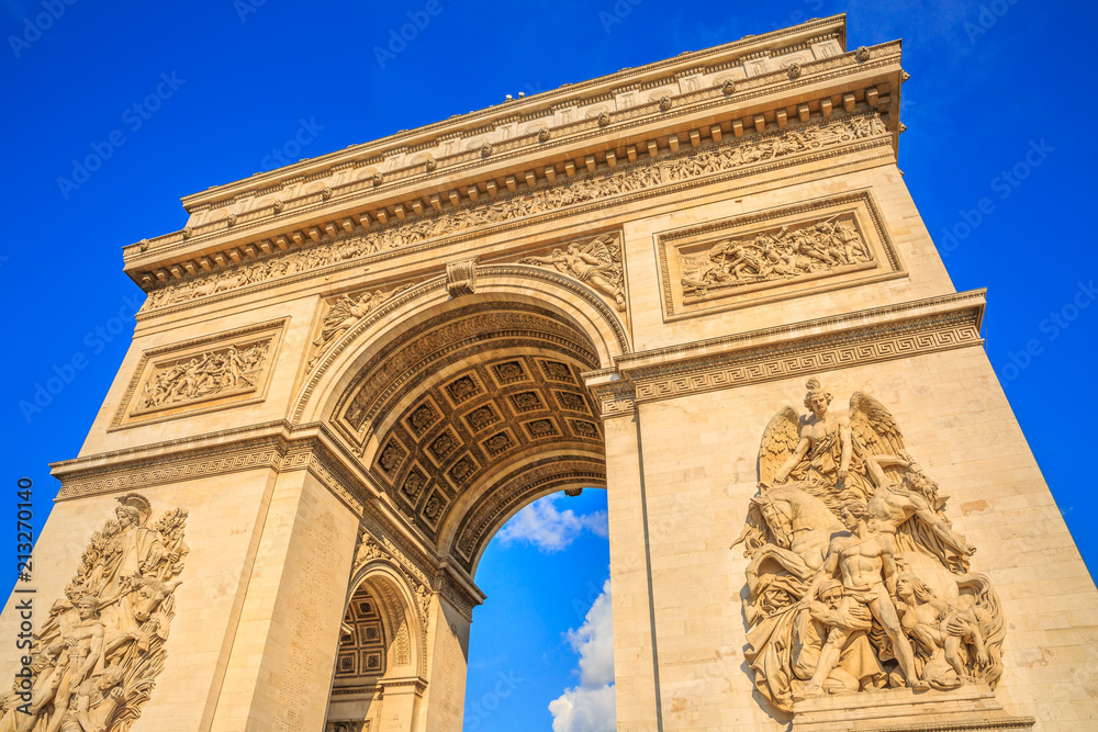 Bottom view of Arch of Triumph at center of Place Charles de Gaulle in a beautiful sunny day with blue sky. Popular landmark and famous tourist attraction in Paris capital of France in Europe.