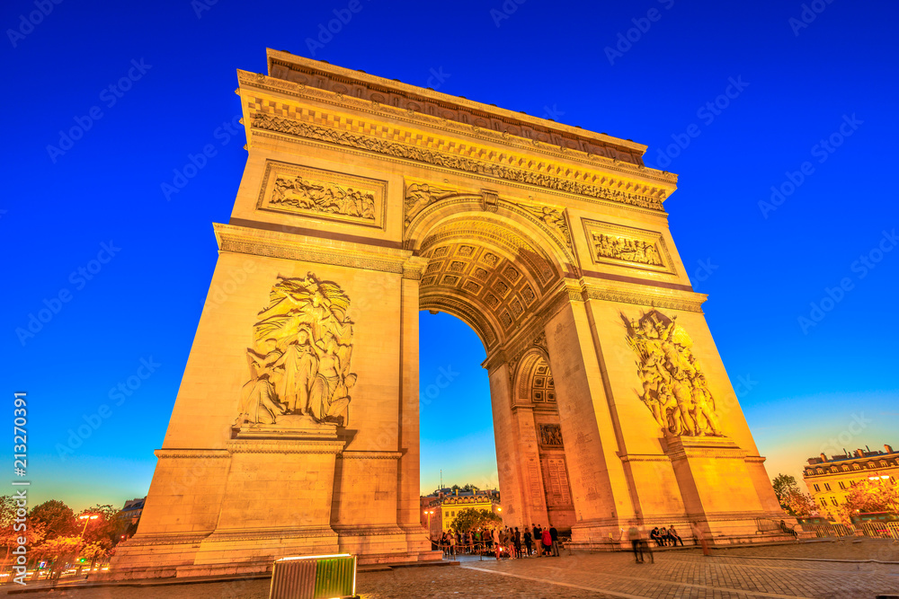 Night view of Arch of Triumph at the center of the Place Charles de Gaulle. Bottom view of popular landmark at blue hour and famous tourist attraction in Paris capital of France in Europe.