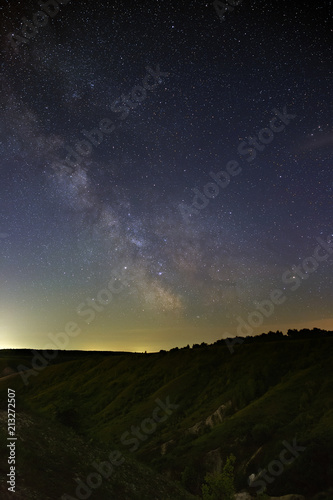 The stars of the Milky Way in the night sky over a hilly landscape. The cosmic space is photographed on a long exposure.