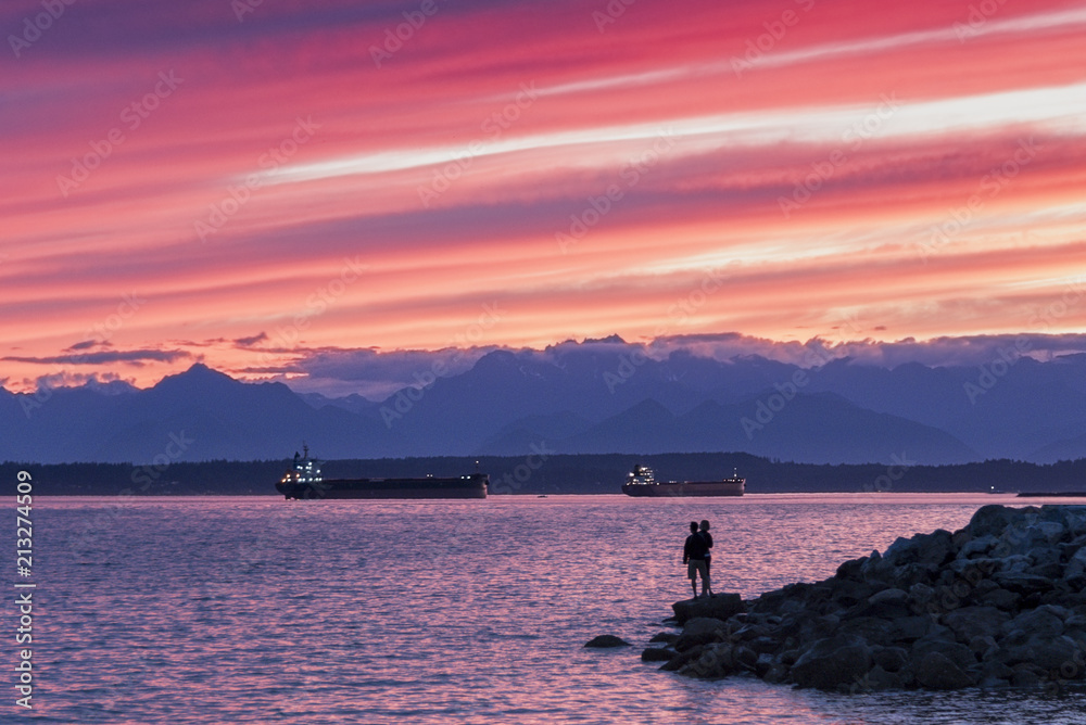 Silhouetted couple at sunset looking out at a glorious sunset with cargo ships next to the Olympic Mountains on Puget Sound