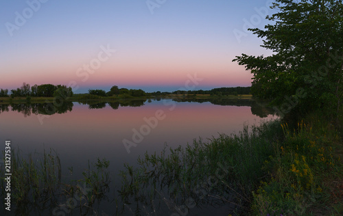 The morning sky is reflected in the smooth surface of the lake. View of the landscape in summer in Russia.