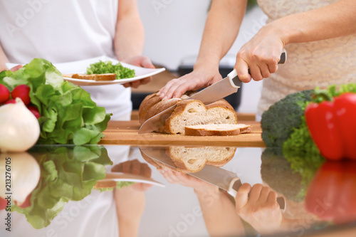 Closeup of human hands cooking in kitchen. Mother and daughter or two female friends cutting bread. Healthy meal, vegetarian food and lifestyle concept