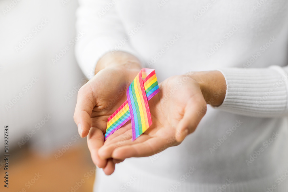 homosexual and lgbt concept - close up of female hands holding gay pride awareness ribbon