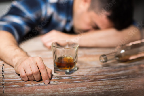 alcoholism  alcohol addiction and people concept - male alcoholic with glass of whiskey and bottle lying or sleeping on table at night