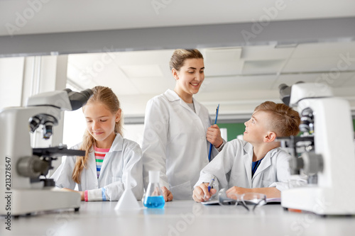 education  science and children concept - teacher and students studying chemistry at school laboratory and writing to workbooks