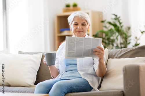 old age, leisure and people concept - happy senior woman drinking coffee or tea and reading newspaper at home © Syda Productions
