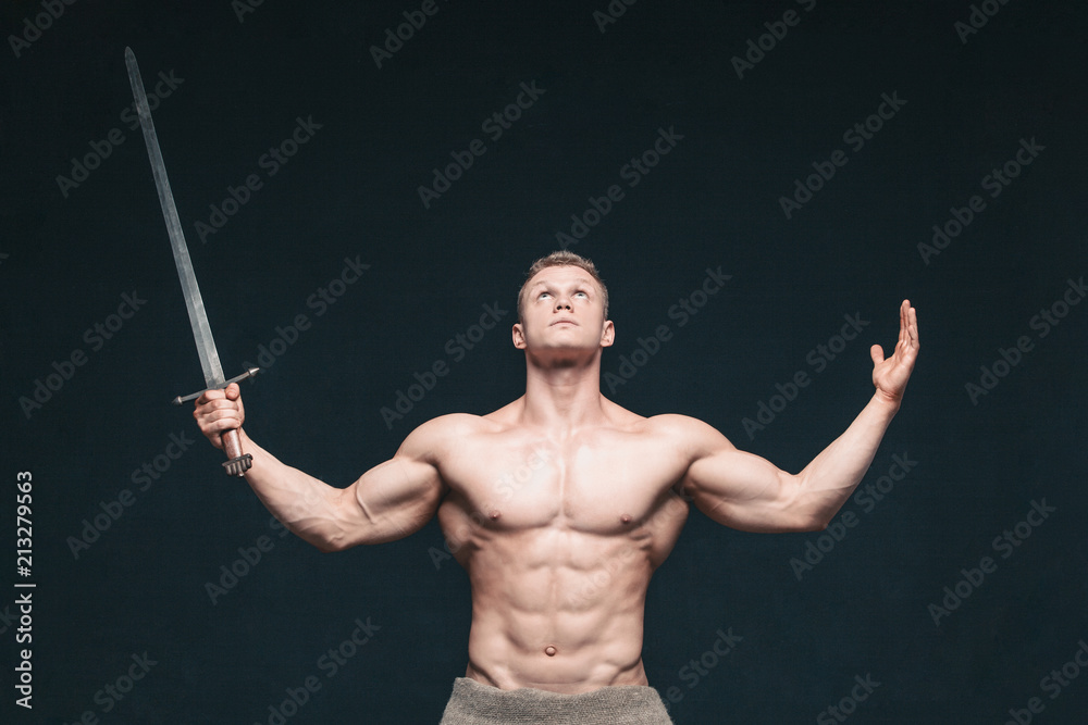 Bodybuilder man posing with a sword isolated on black background