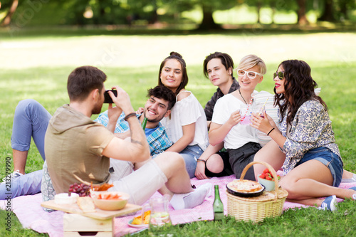 friendship  leisure and technology concept - group of happy smiling friends with non alcoholic drinks photographing at picnic in summer park