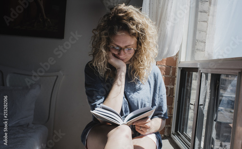 Woman reading book while sitting on window sill at home photo