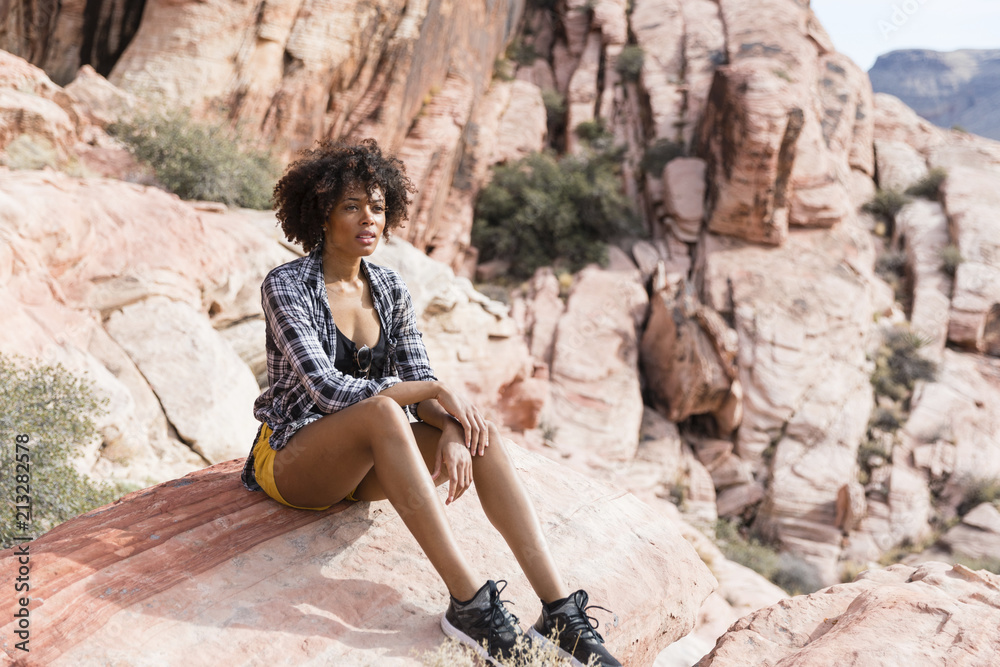 Thoughtful woman looking away while sitting on rock formation during sunny day Thoughtful woman looking away while sitting on rock formation during sunny day