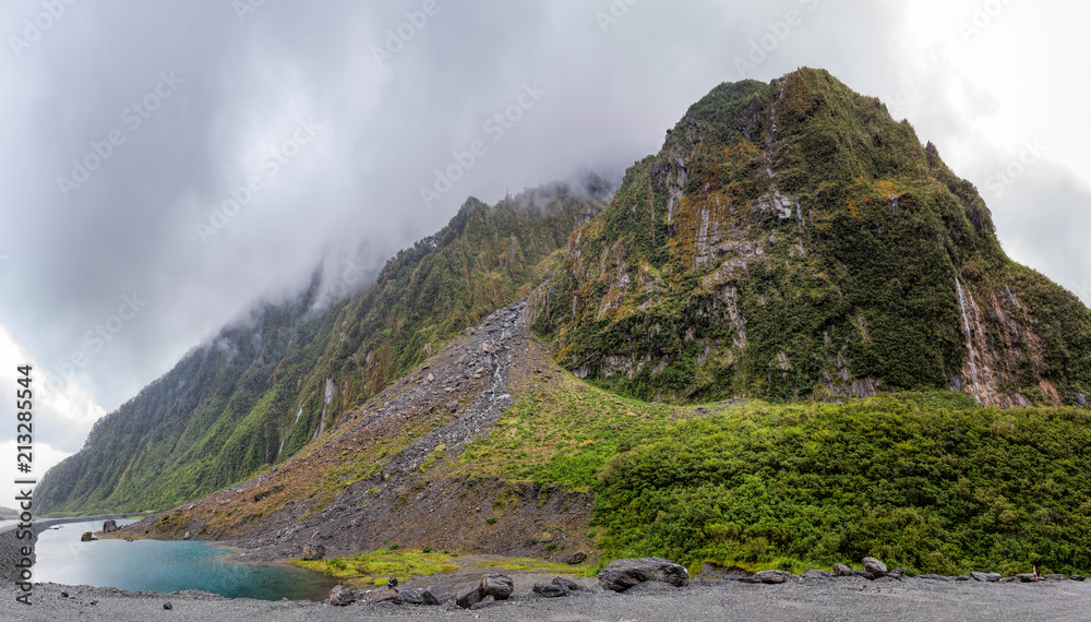 Obraz premium Rockface with waterfalls and a small lake near Fox Glacier on New Zealand's south island.