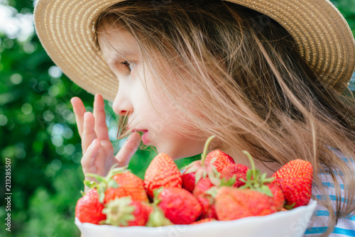 happy baby girl holding a plate of strawberries in her hands. 