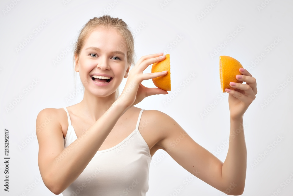 Beautiful young blonde woman in white shirt holding piece of orange near her head smiling Beautiful young blonde woman in white shirt holding piece of orange near her head smiling