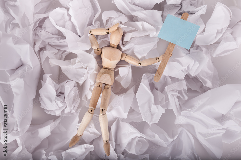 Jointed manikin doll overwhelmed hand on head holding a blank sign on crumbled balls of paper Jointed manikin doll overwhelmed hand on head holding a blank sign on crumbled balls of paper