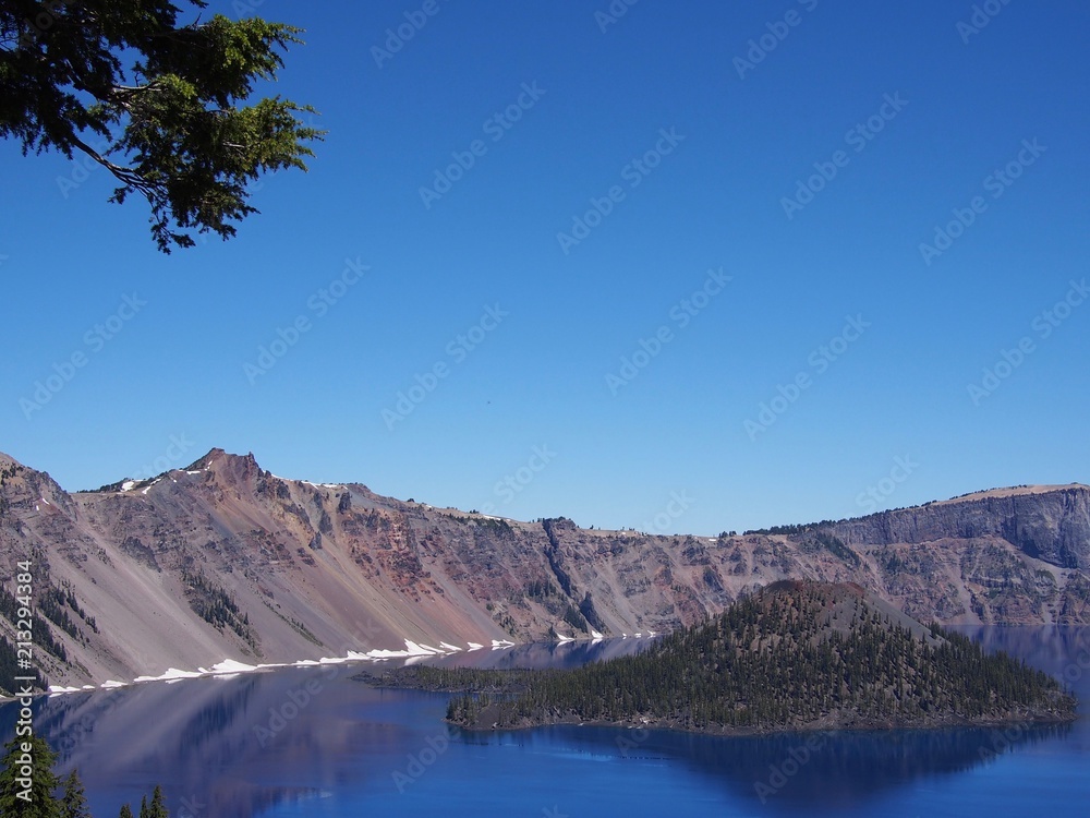 Fototapeta premium The magnificent rich blue waters of Crater Lake with reflections of the rim in the forests of Southern Oregon on a beautiful sunny summer morning. 
