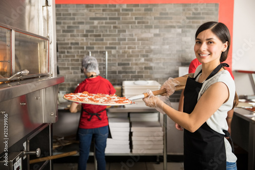 Female cook putting fresh made pizza in oven