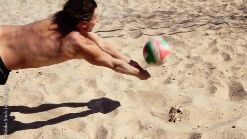 Beach volleyball player in action. Man beats the ball in a jump on the beach in slow motion. Beach volleyball player diving for the ball.